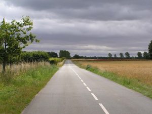 Route secondaire filant vers l'horizon, sous un plafond bas de nuages.